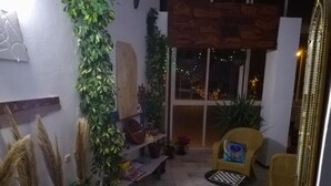 Un espacio interior acogedor con una mesa a cuadros, sillas de mimbre y plantas en macetas.