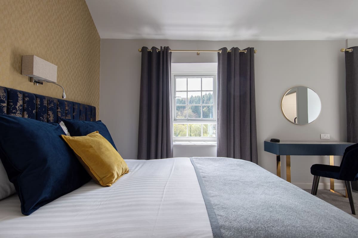 A hotel room with a bed, a desk, a chair, a mirror, and a window with curtains.