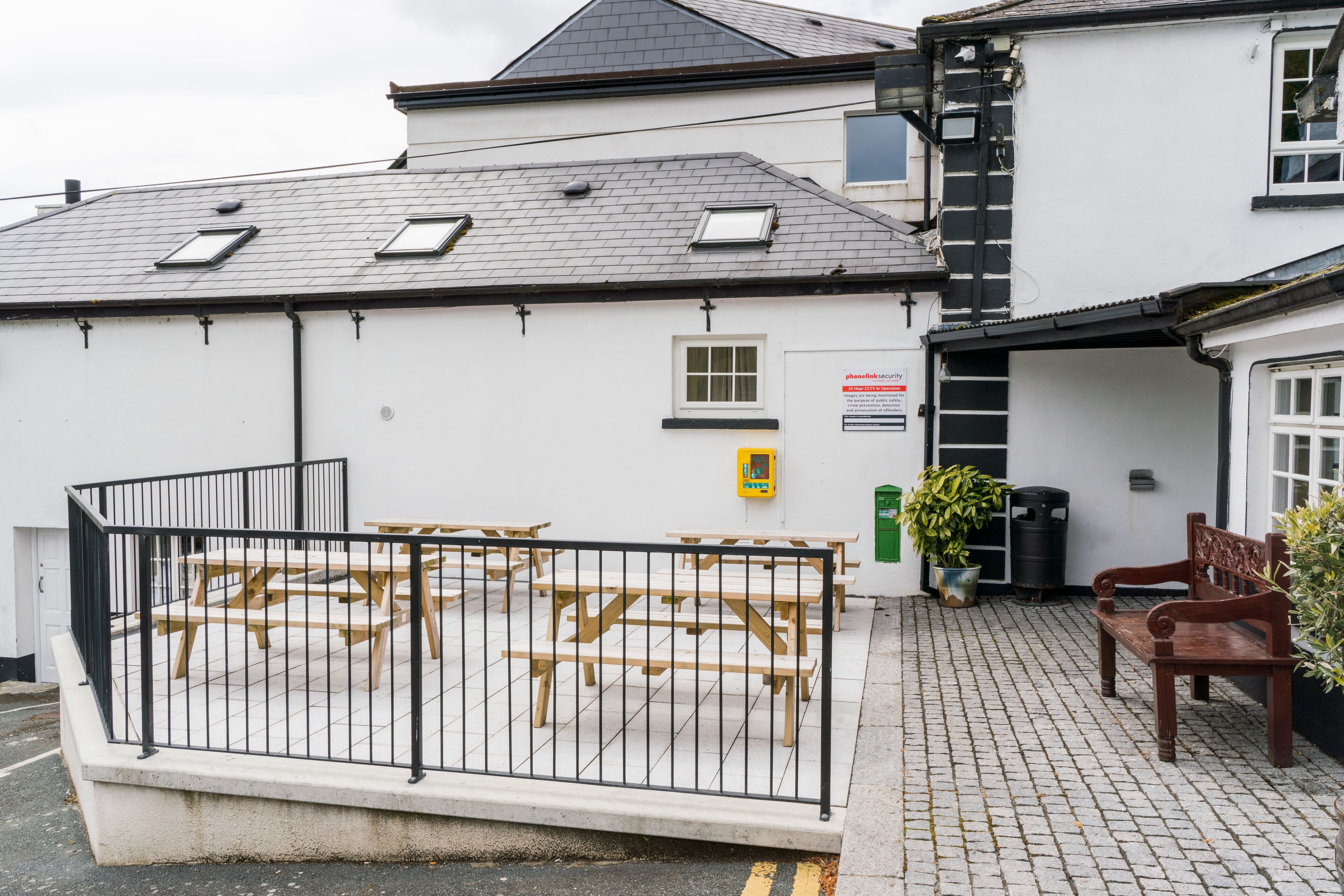 A building with a white exterior, a tiled patio area with wooden benches, and a black metal fence.