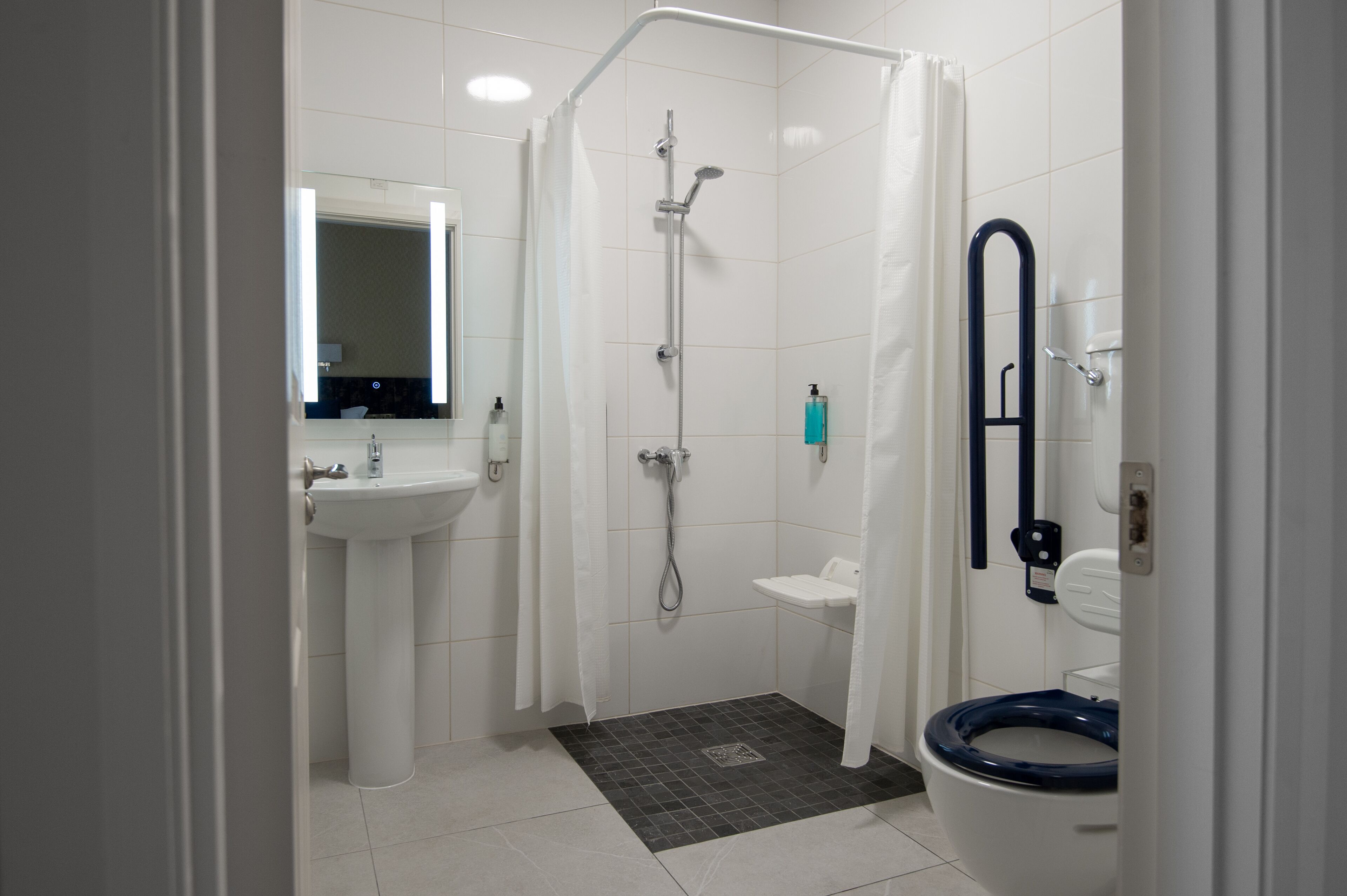 A bathroom with a shower, toilet, sink, and a mirror.