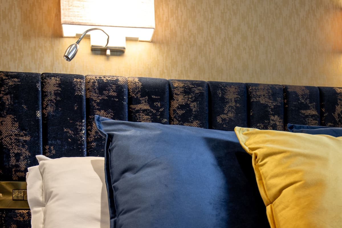 A neatly made bed with a headboard, a wall-mounted lamp, and a textured wall.