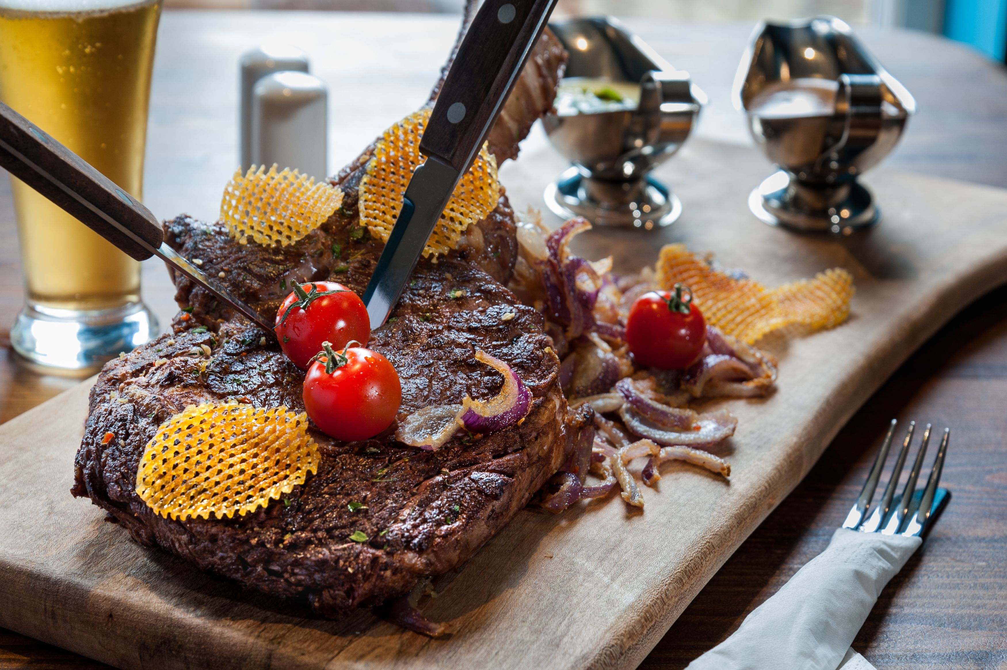 Un bistec con un cuchillo, tomates y cebollas sobre una tabla de madera.