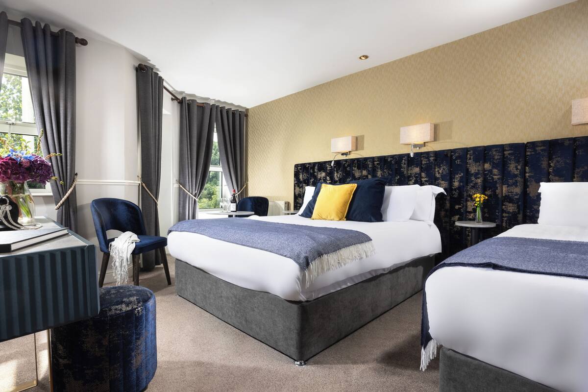 A hotel room with two beds, a desk, a chair, and a view of the outdoors.