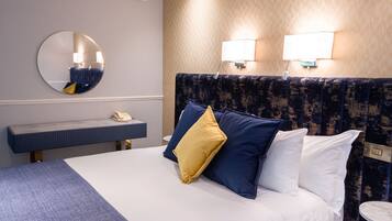 A hotel room with a bed, a round mirror, a bedside table with a phone, and two wall-mounted lamps.