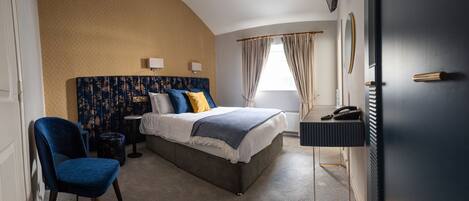 A bedroom with a curved wall, a bed with a headboard, a bedside table, a chair, a desk with a telephone, and a window with curtains.