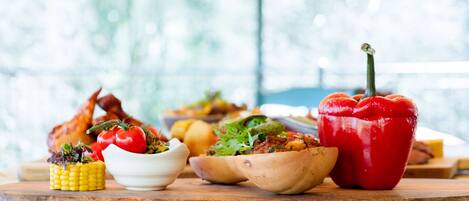 A wooden table with various dishes including corn, tomatoes, and a red bell pepper.