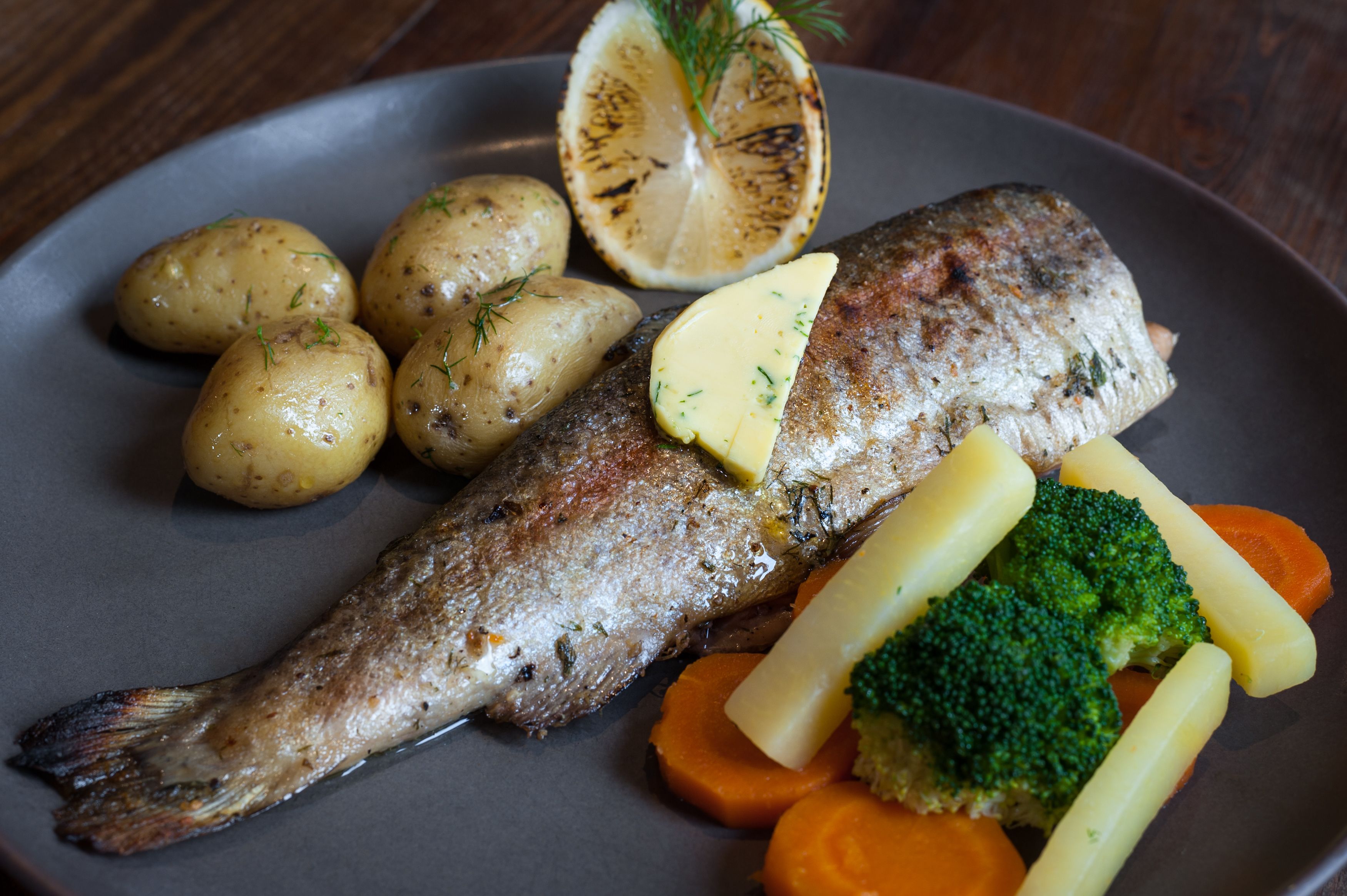 A plate with grilled fish, potatoes, carrots, and a lemon slice.