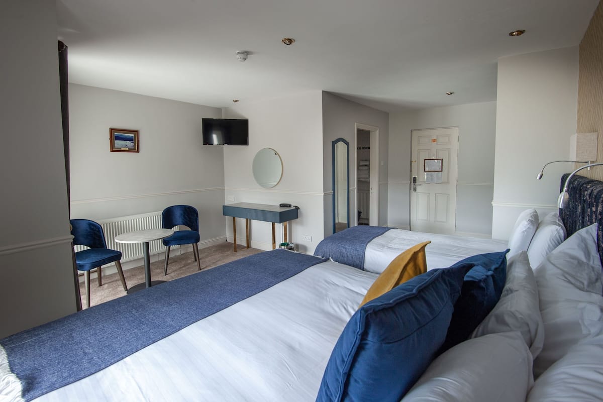 A hotel room with two beds, a desk, a chair, a TV, and a mirror.