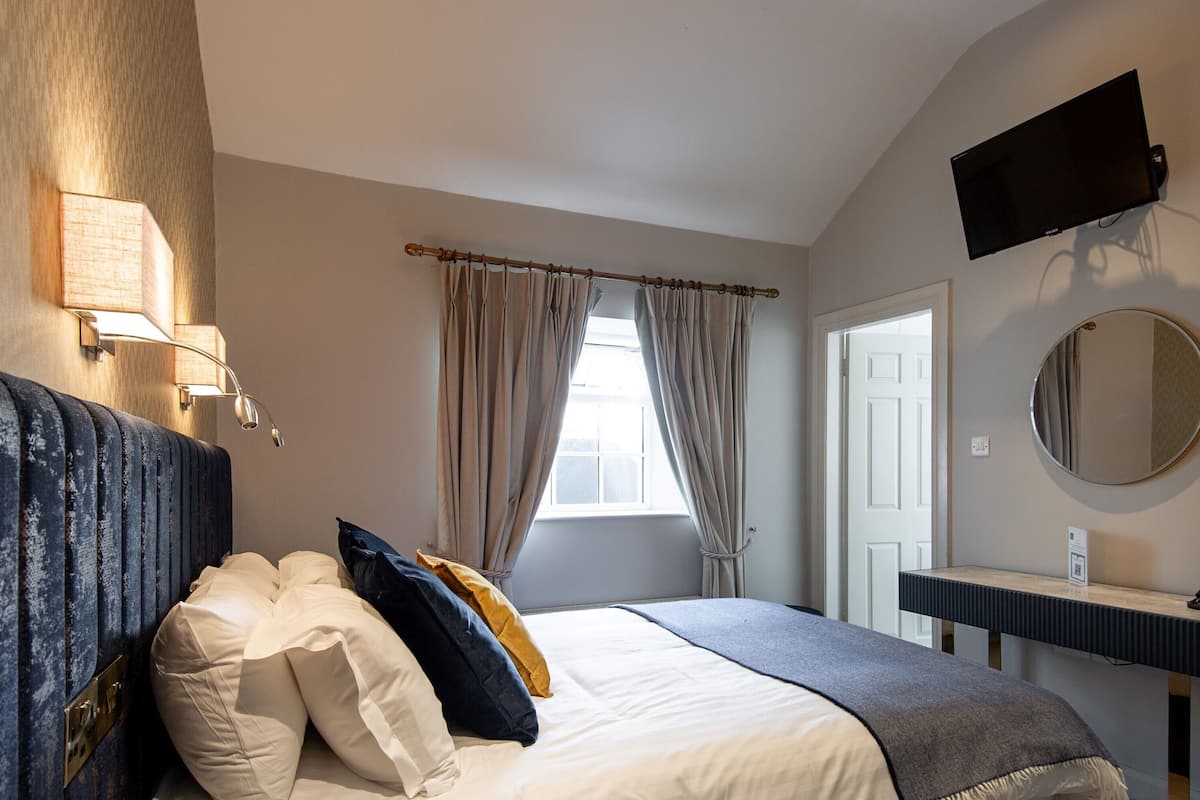 A bedroom with a bed, bedside lamps, a TV, a mirror, and a bathroom door.