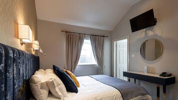 A bedroom with a bed, bedside lamps, a TV, a mirror, and a bathroom door.