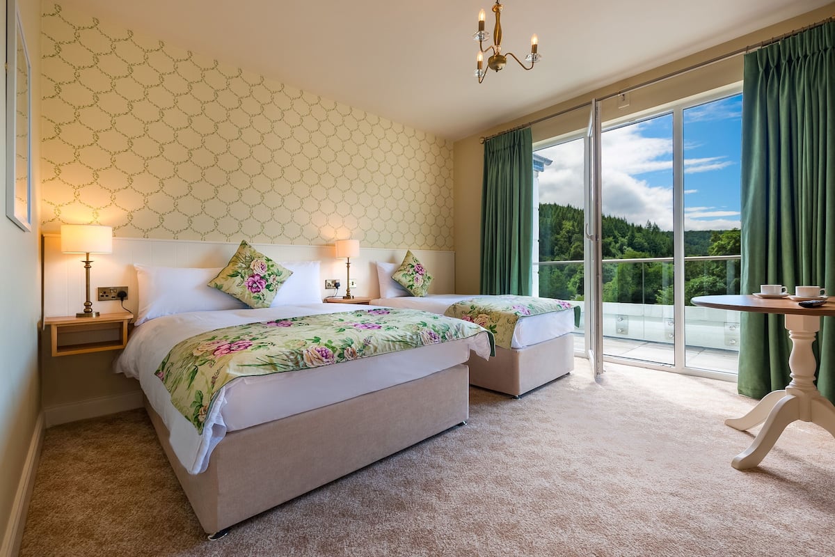 A hotel room with two beds, a balcony with a view, and a table with cups.