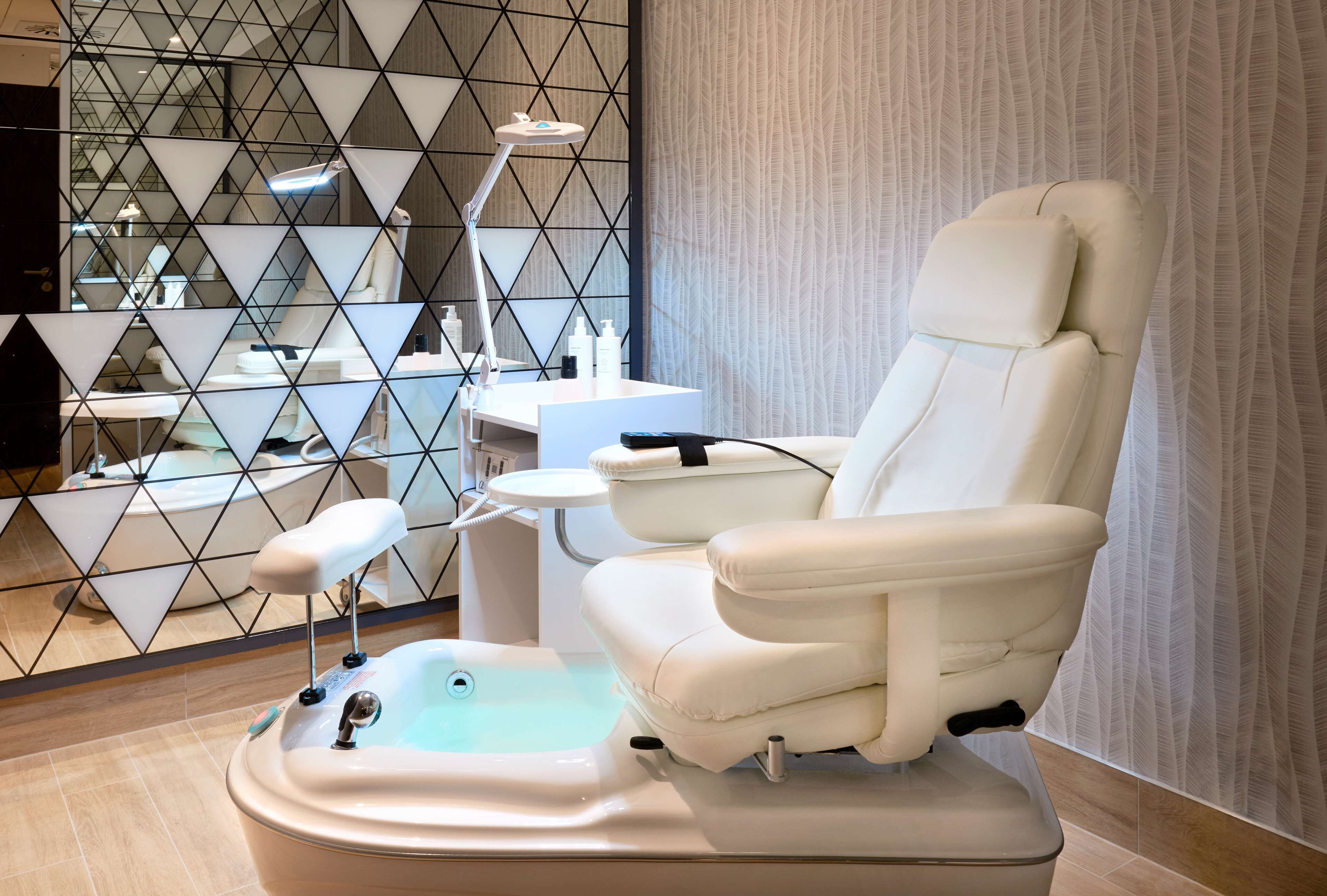 A modern spa room with a massage chair, a foot bath, and a small table with a lamp.