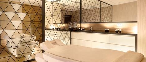 A modern spa room with a massage table, a wooden floor, and a geometric-patterned partition.
