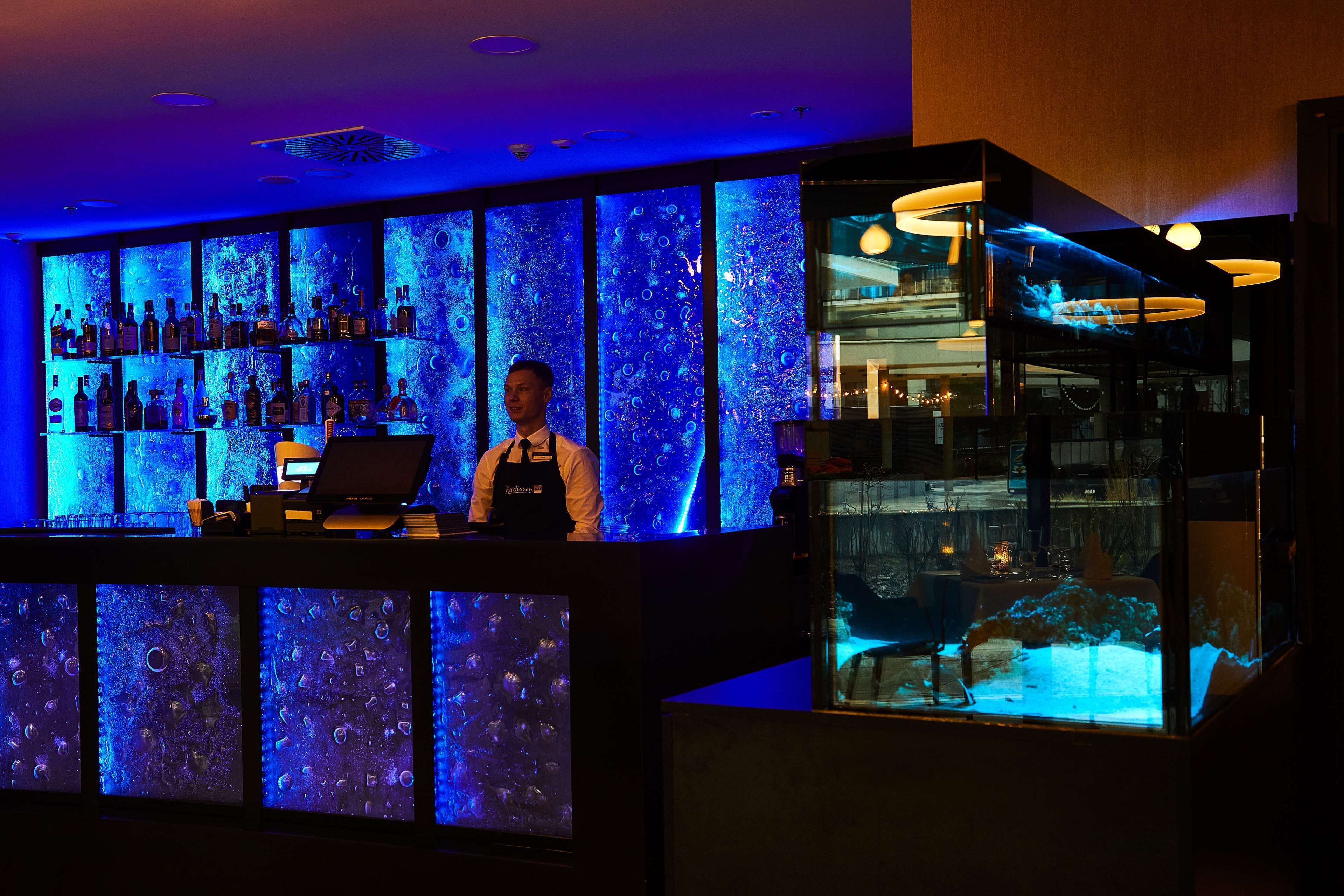 A bar area with shelves of bottles, a bartender, and a large aquarium display.