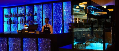 A bar area with shelves of bottles, a bartender, and a large aquarium display.