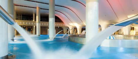 Una piscina interior moderna con un diseño arquitectónico único, que presenta techos curvos y múltiples columnas.