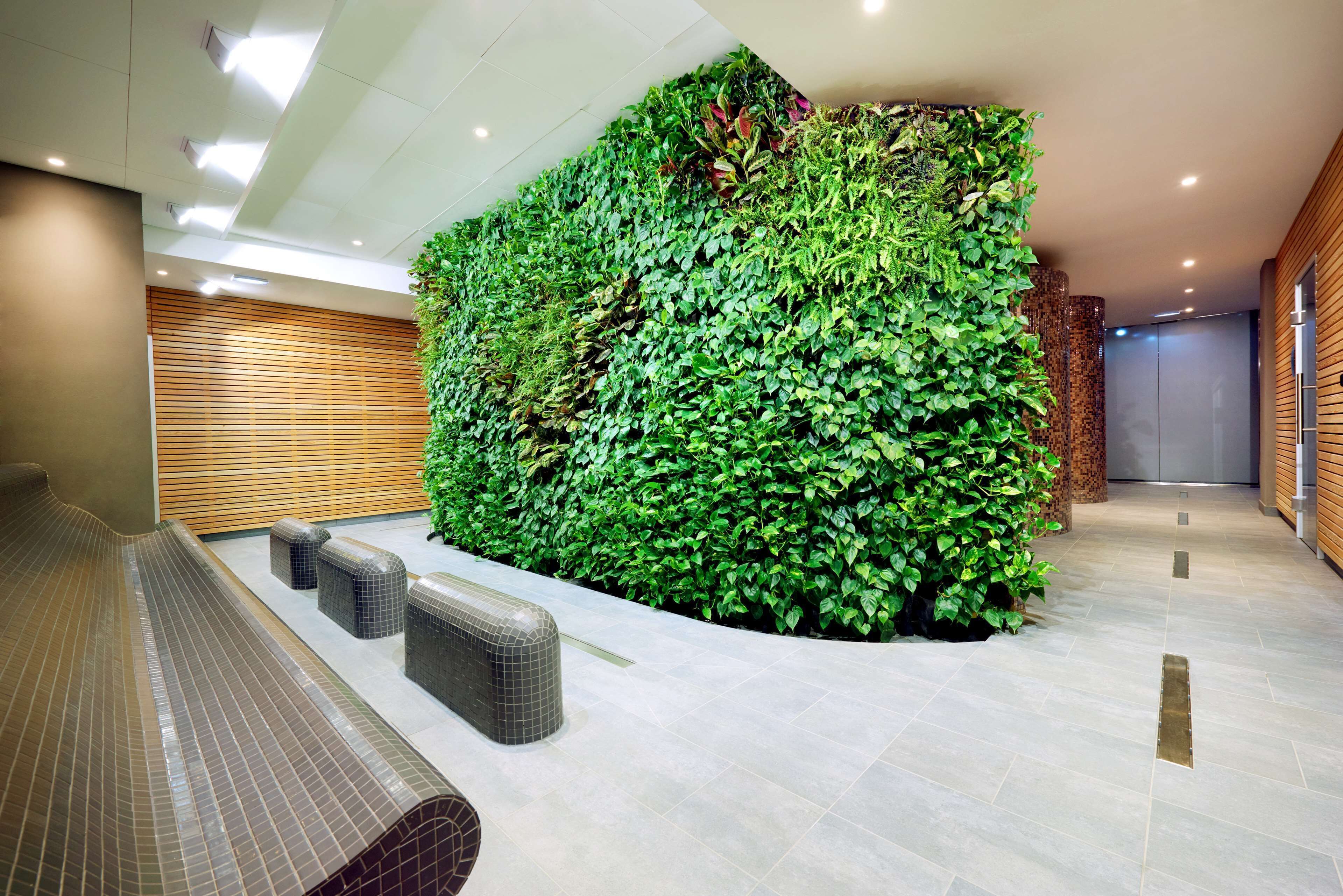 A modern lobby with a green vertical garden wall, tiled flooring, and a seating area with benches.