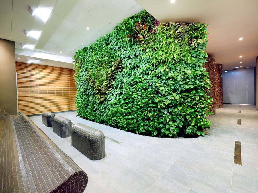 Un vestíbulo moderno con un jardín vertical verde, suelo de baldosas y una zona de estar con bancos.