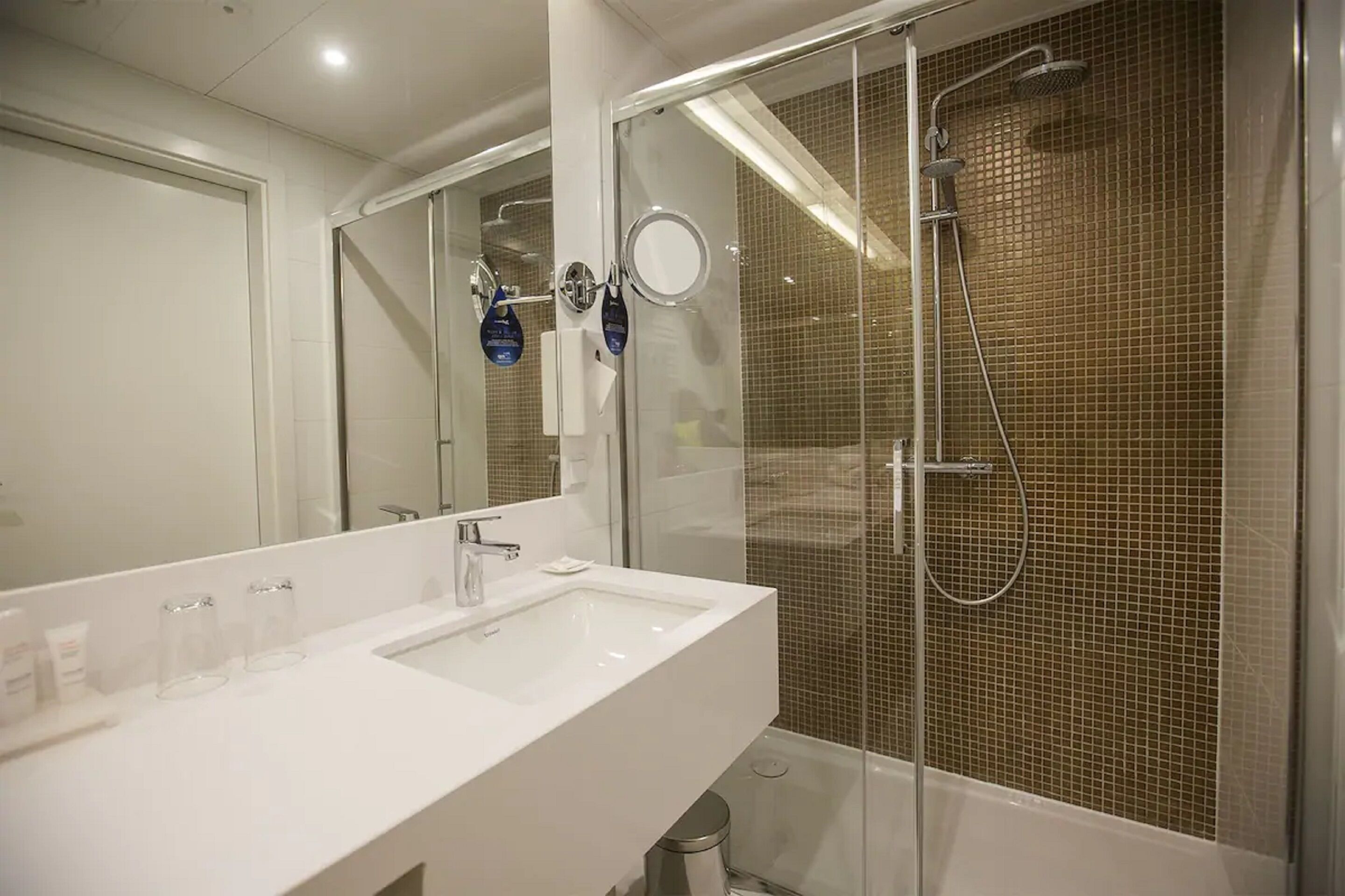 A modern bathroom with a white sink, a glass-enclosed shower, and a tiled wall.