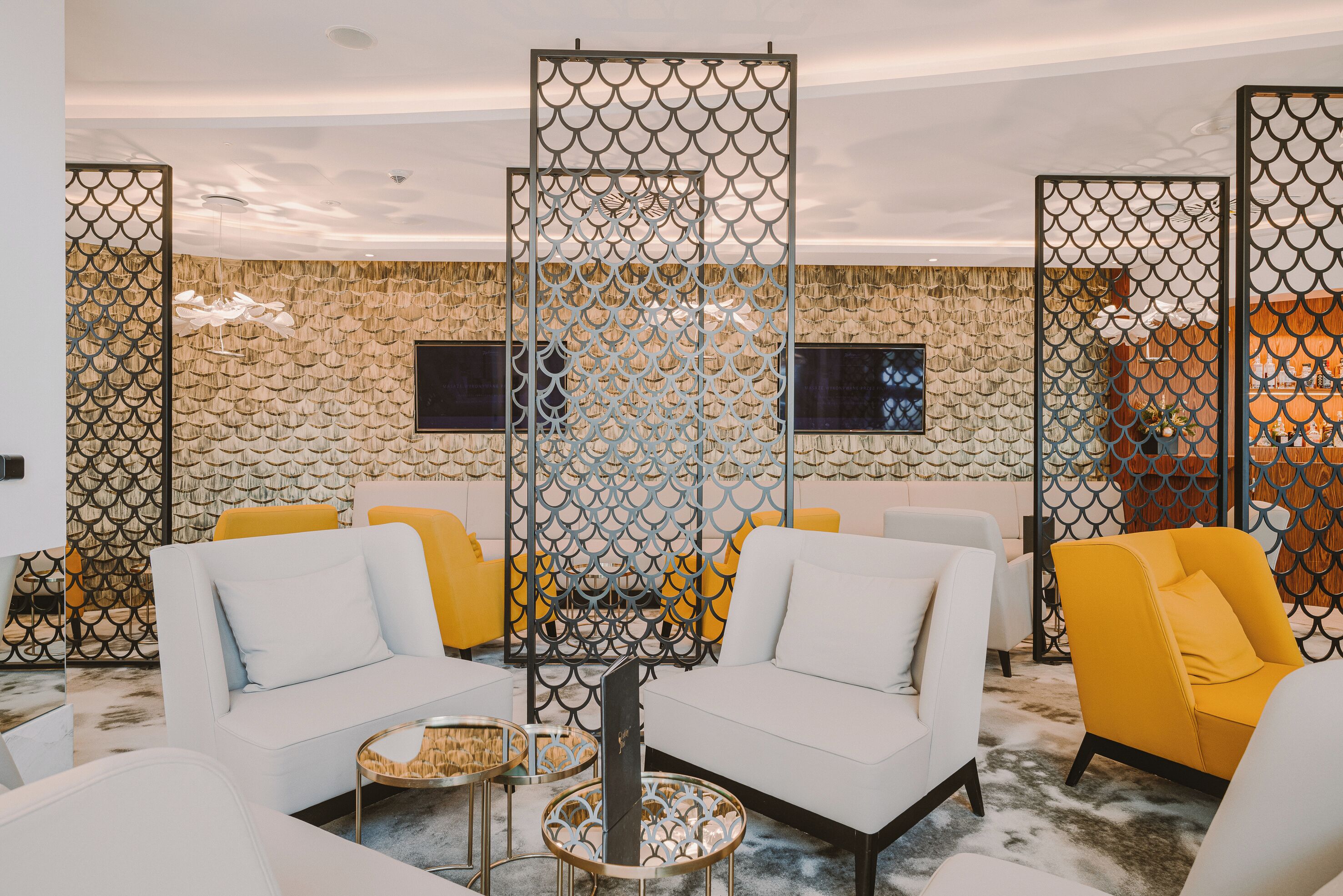 A modern lounge area with white sofas, yellow chairs, and a patterned wall.