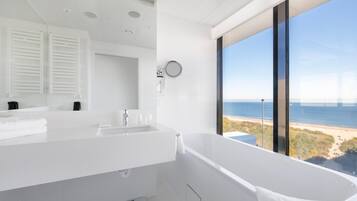 Une salle de bain moderne dotée d’une grande baignoire, d’un lavabo double et d’une grande fenêtre donnant sur la plage.