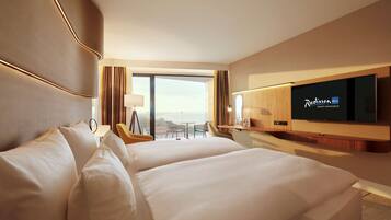 A hotel room with two beds, a TV, a desk, and a view of the outdoors.