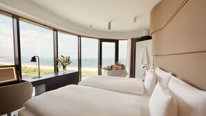 Ein Hotelzimmer mit einem großen Bett, einem Schreibtisch und Blick auf den Strand.