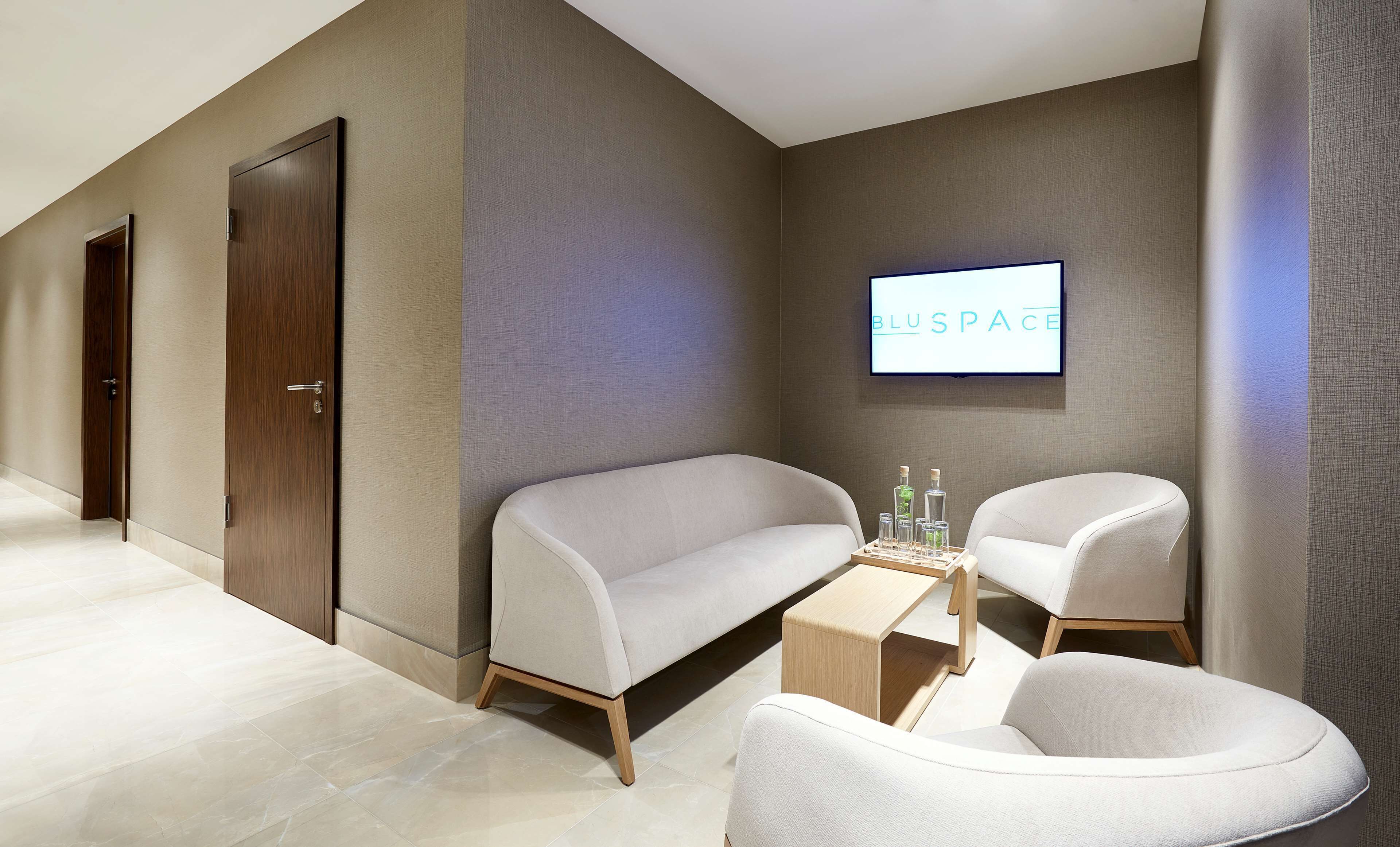 A modern hotel lobby with a reception desk, two sofas, and a wall-mounted TV displaying 'BLUSPACE'.
