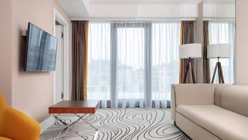 Ein Hotelzimmer mit einer Couch, einem kleinen Tisch, einem an der Wand befestigten Fernseher und einem Fenster mit Vorhängen.