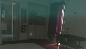 Ein Hotelzimmer mit einem großen Bett, einem Schreibtisch und einem Sessel. Eine Tür führt zu einem Badezimmer und einer Küchenzeile.