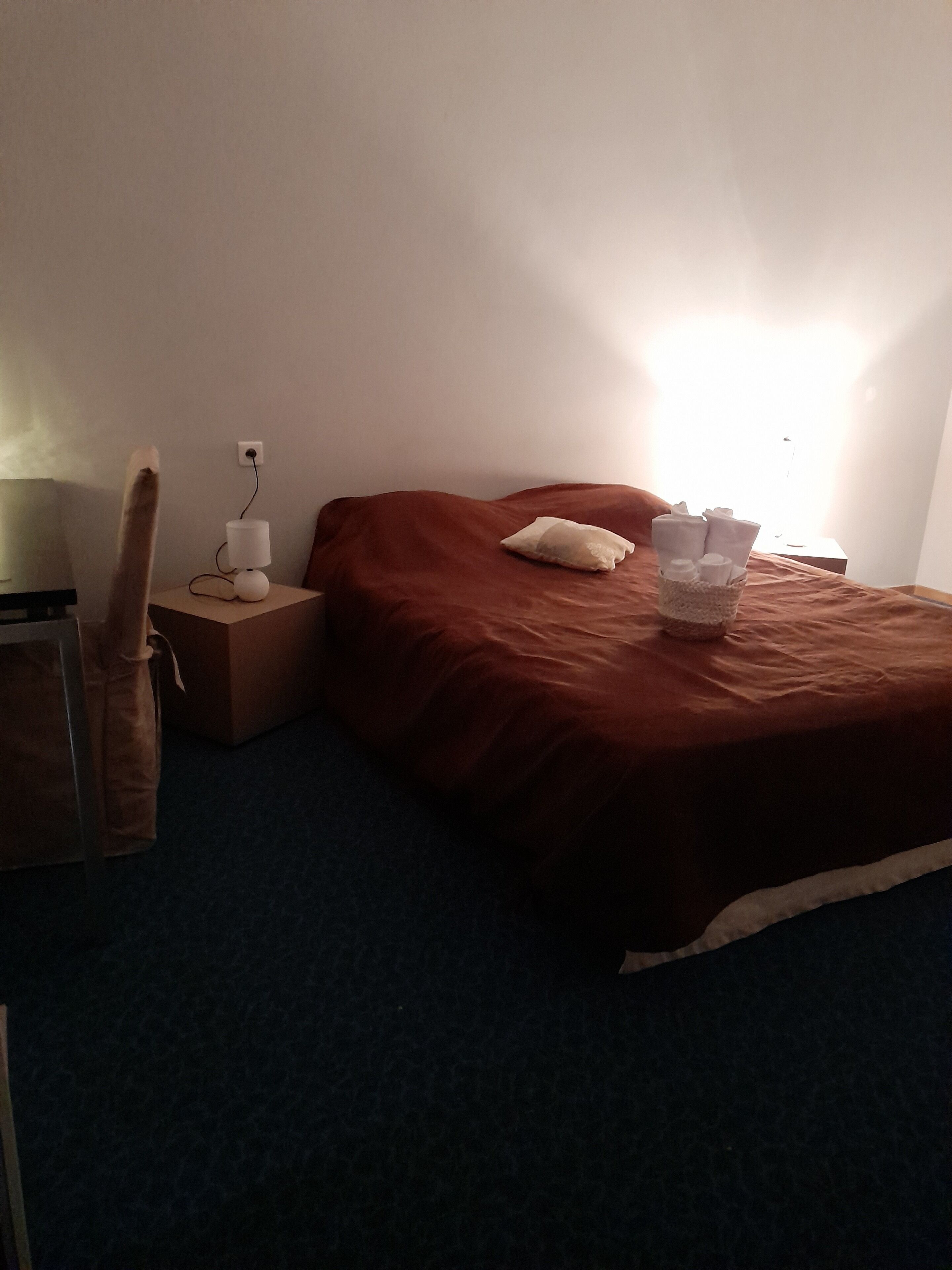 A bedroom with a bed, a nightstand, a lamp, and a suitcase.