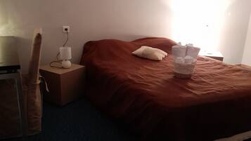 A bedroom with a bed, a nightstand, a lamp, and a suitcase.