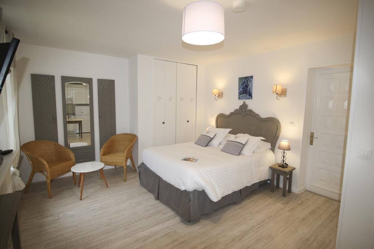 A bedroom with a bed, two chairs, a small table, a wardrobe, and a door.