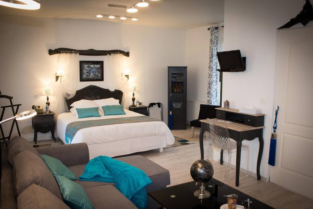 A bedroom with a bed, bedside tables, a desk, a chair, a globe, and a TV on the wall.