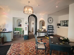 A spacious living room with a large chandelier, a green sofa, a patterned rug, and a dining area with a table and chairs. - Au Clos Paillé La Roche-Posay (La Roche-Posay)