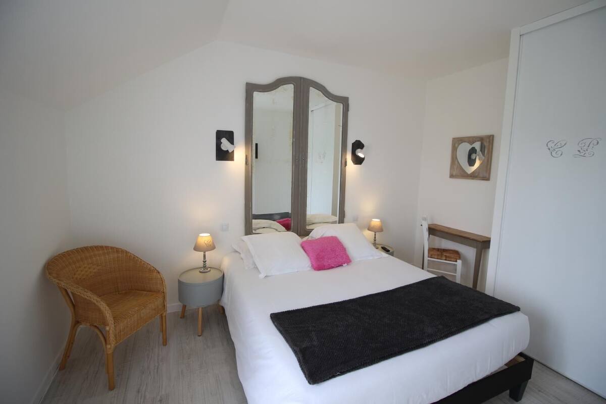 A bedroom with a bed, two bedside tables, a chair, a mirror, and a wall-mounted picture.