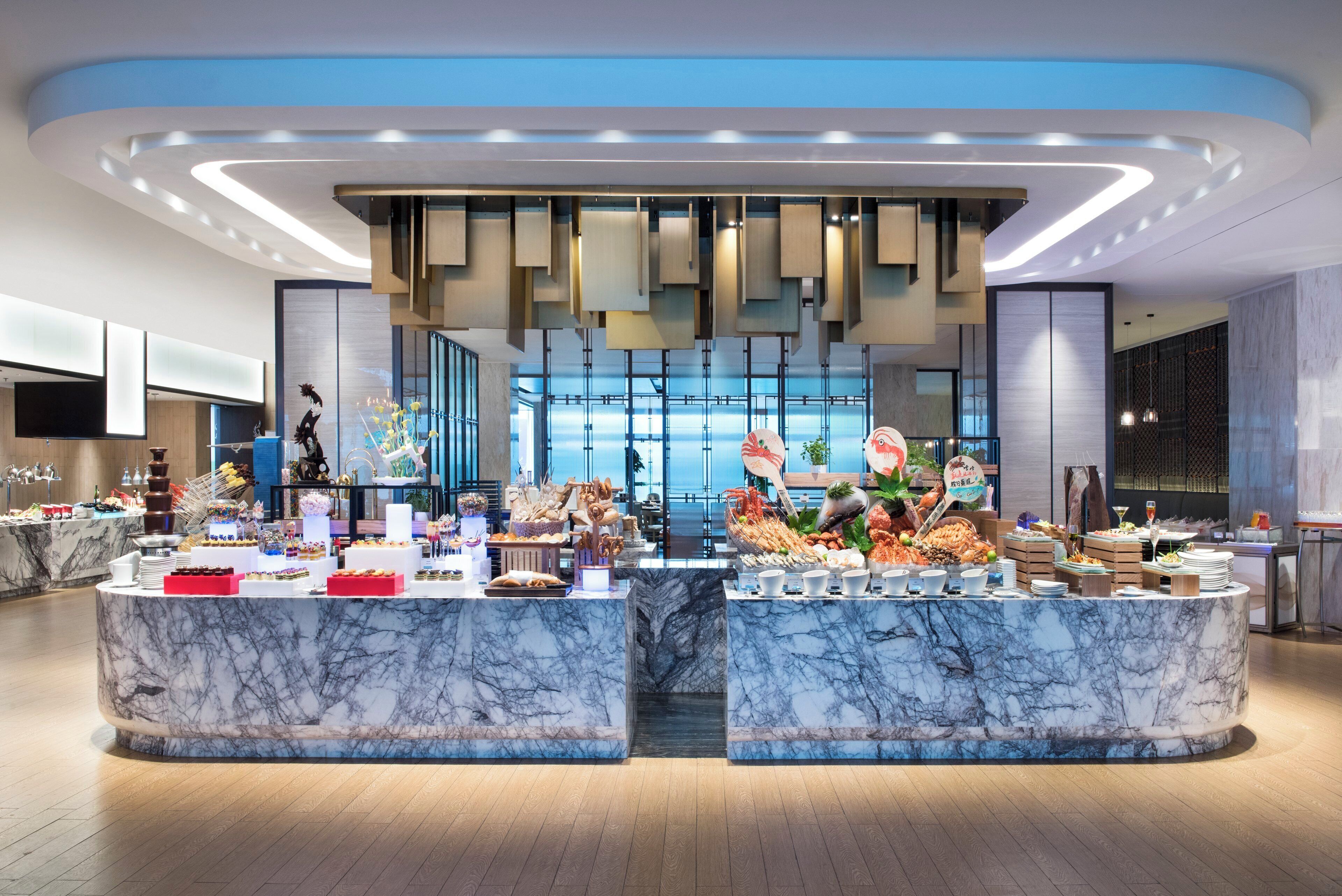 A modern hotel lobby with marble counters, a central reception area, and a view of the cityscape through large windows.