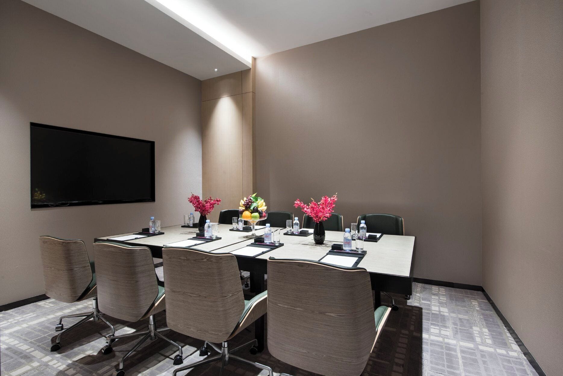 Un salón de conferencias con una larga mesa, sillas, un televisor de pantalla plana y centros de mesa con flores.