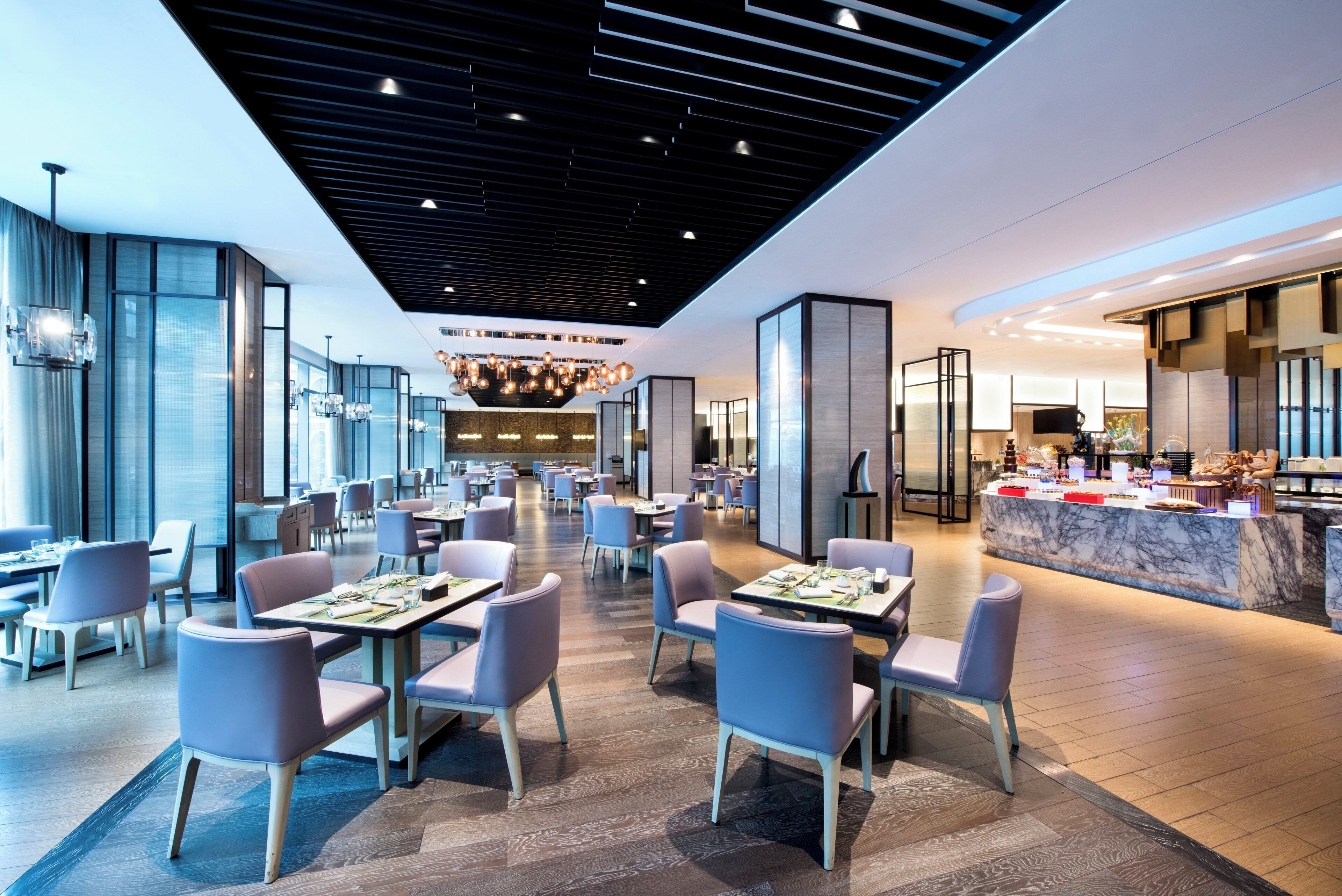 A modern restaurant with a central dining area, a bar, and a kitchen visible in the background.
