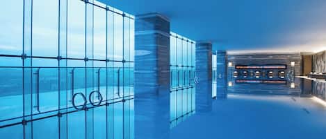 A modern indoor pool with clear glass walls and a view of the cityscape.