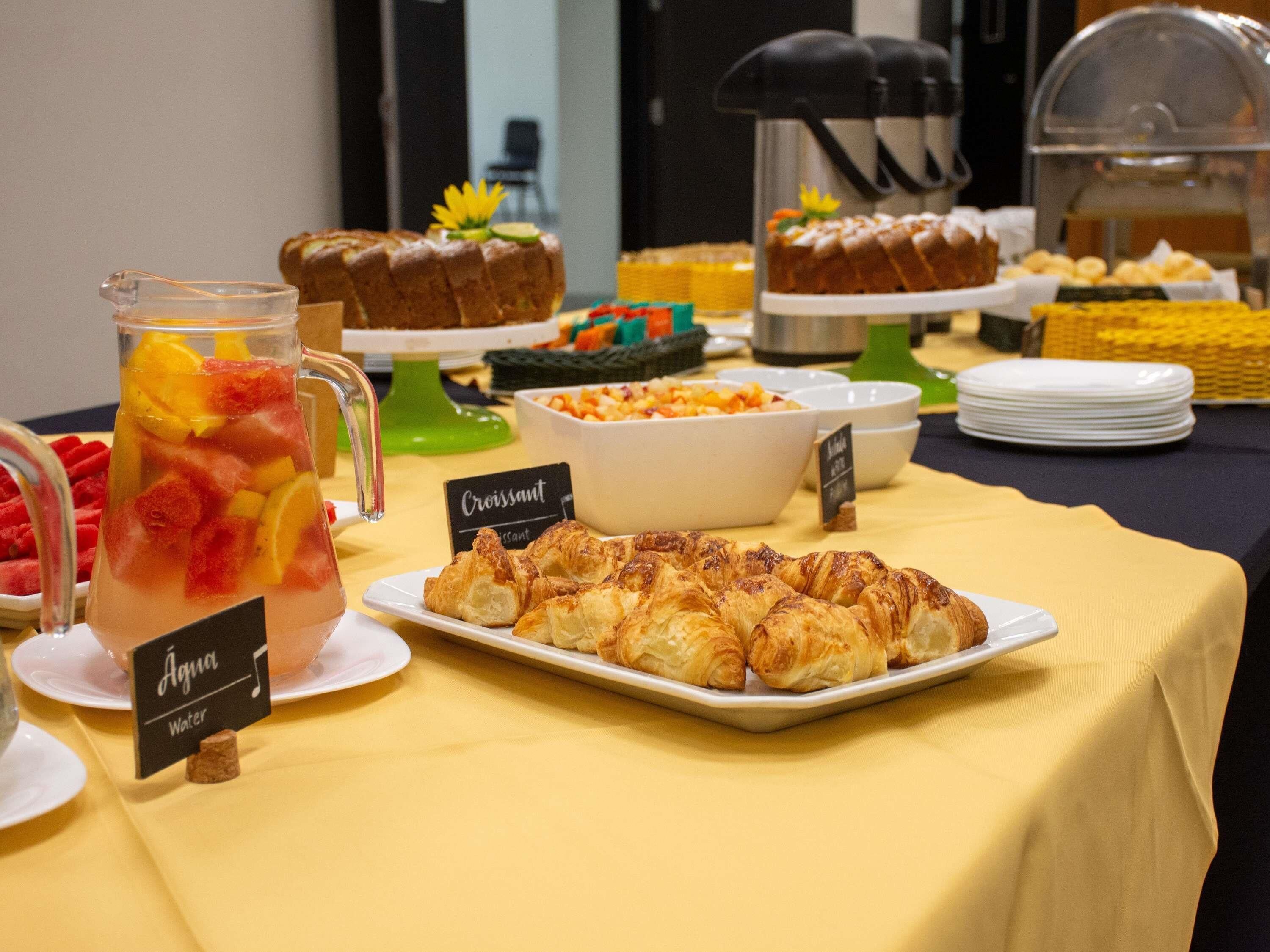 Una mesa de buffet con cruasanes, ponche de frutas y diversos platos.