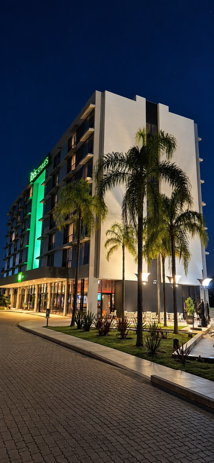 Un hotel moderno con un llamativo letrero verde, varios pisos y una zona de entrada bien iluminada con asientos al aire libre.