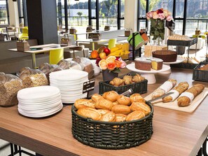 Een buffet met diverse gerechten, waaronder brood, gebak en een taart, in een moderne eetruimte met grote ramen.