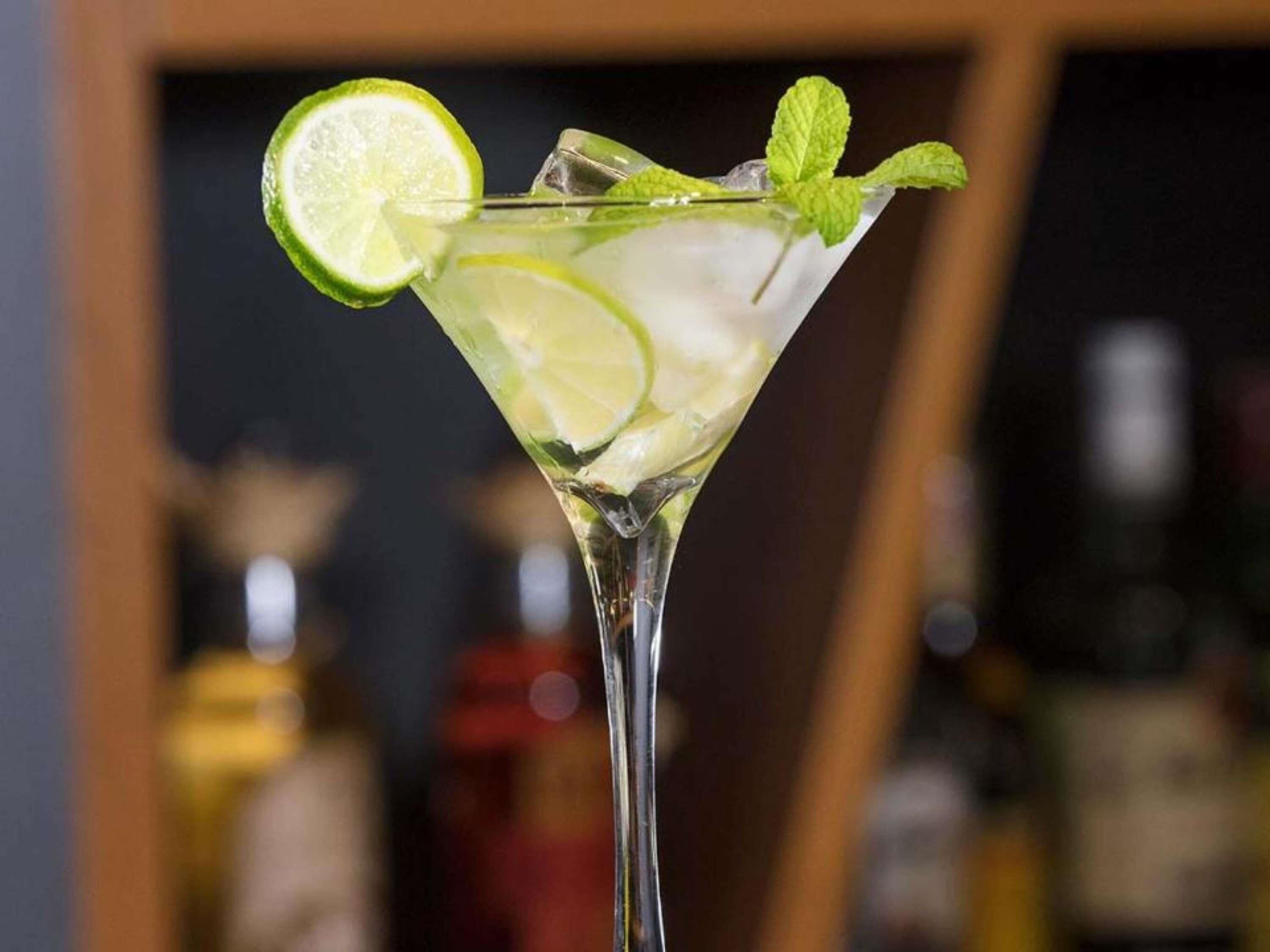 Un cóctel con adorno de lima y menta en una copa de martini.