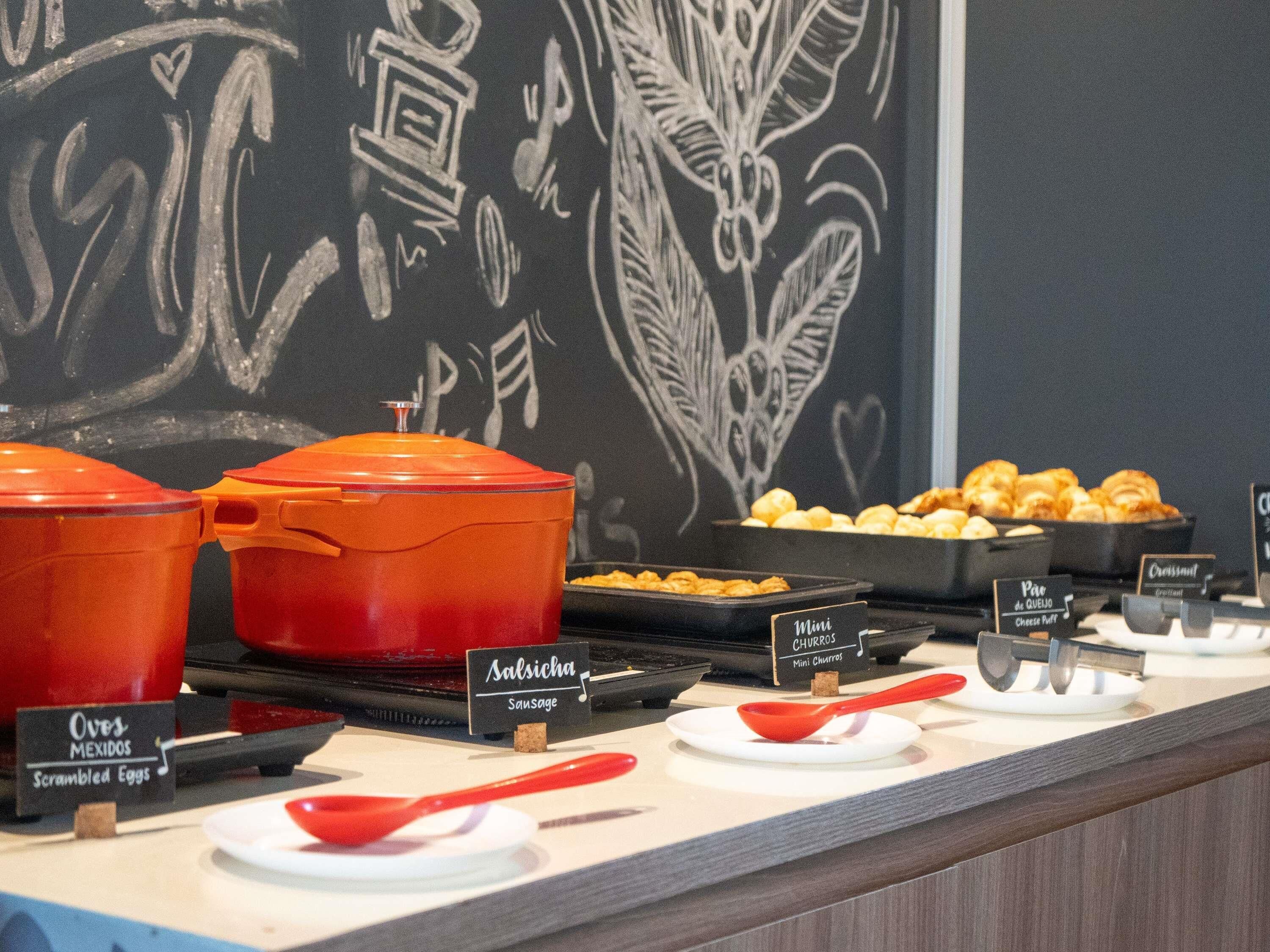 A buffet with labeled dishes including sausages, scrambled eggs, and mini churros.