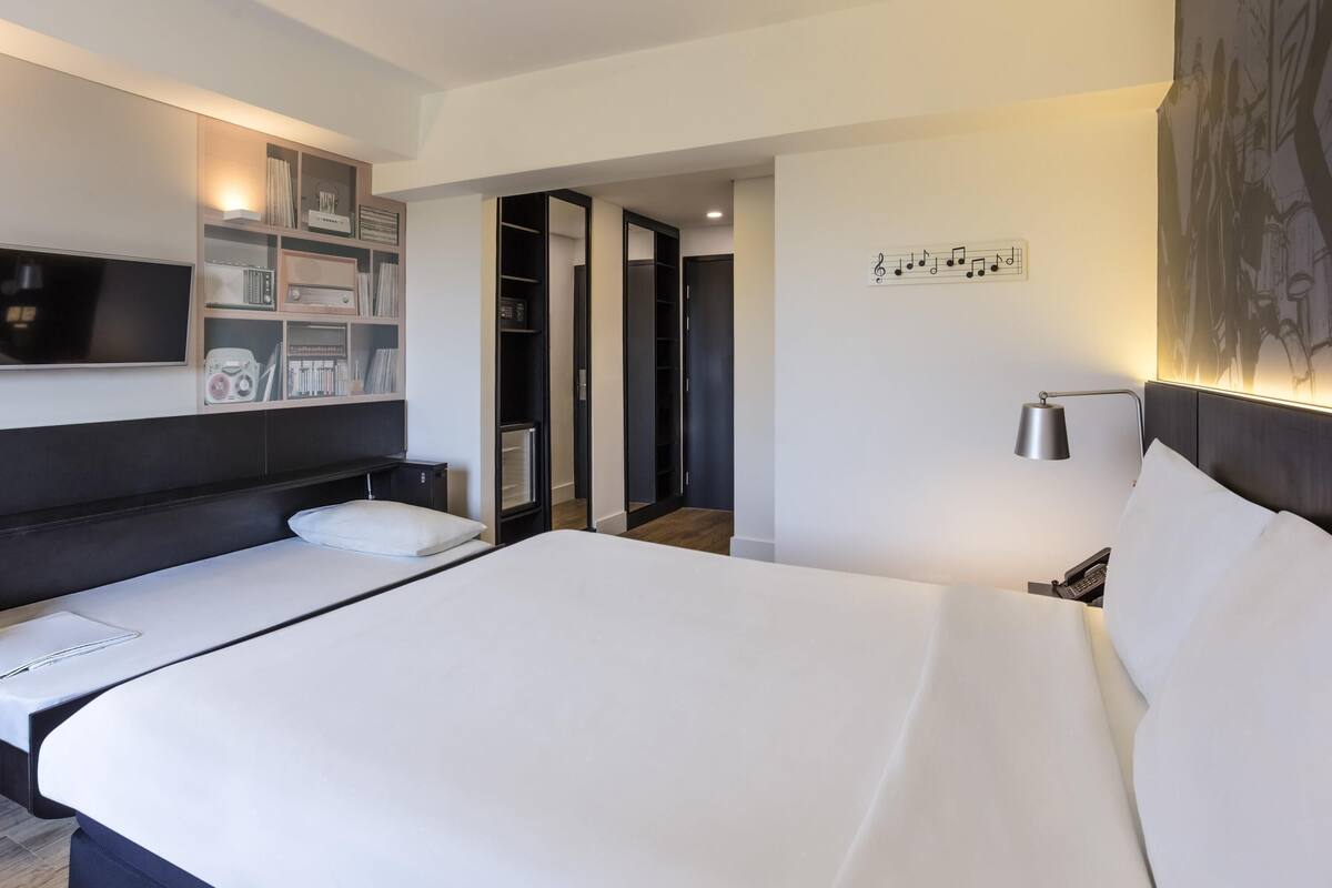 Une chambre d’hôtel avec un grand lit, un téléviseur fixé au mur, une table de chevet, une lampe et une armoire.