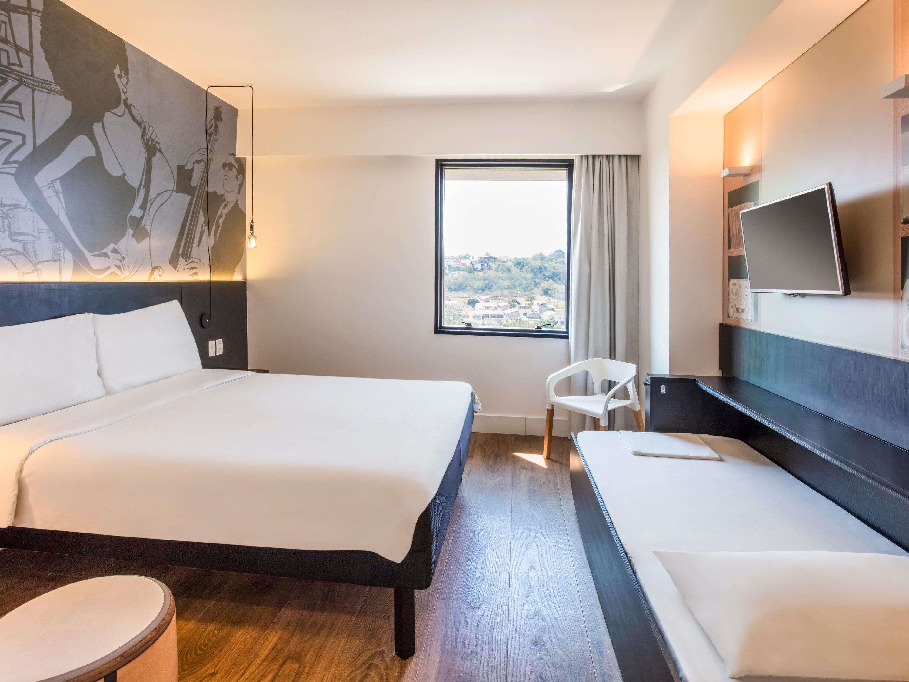 A hotel room with a bed, a desk, a chair, a TV, and a window with a view.