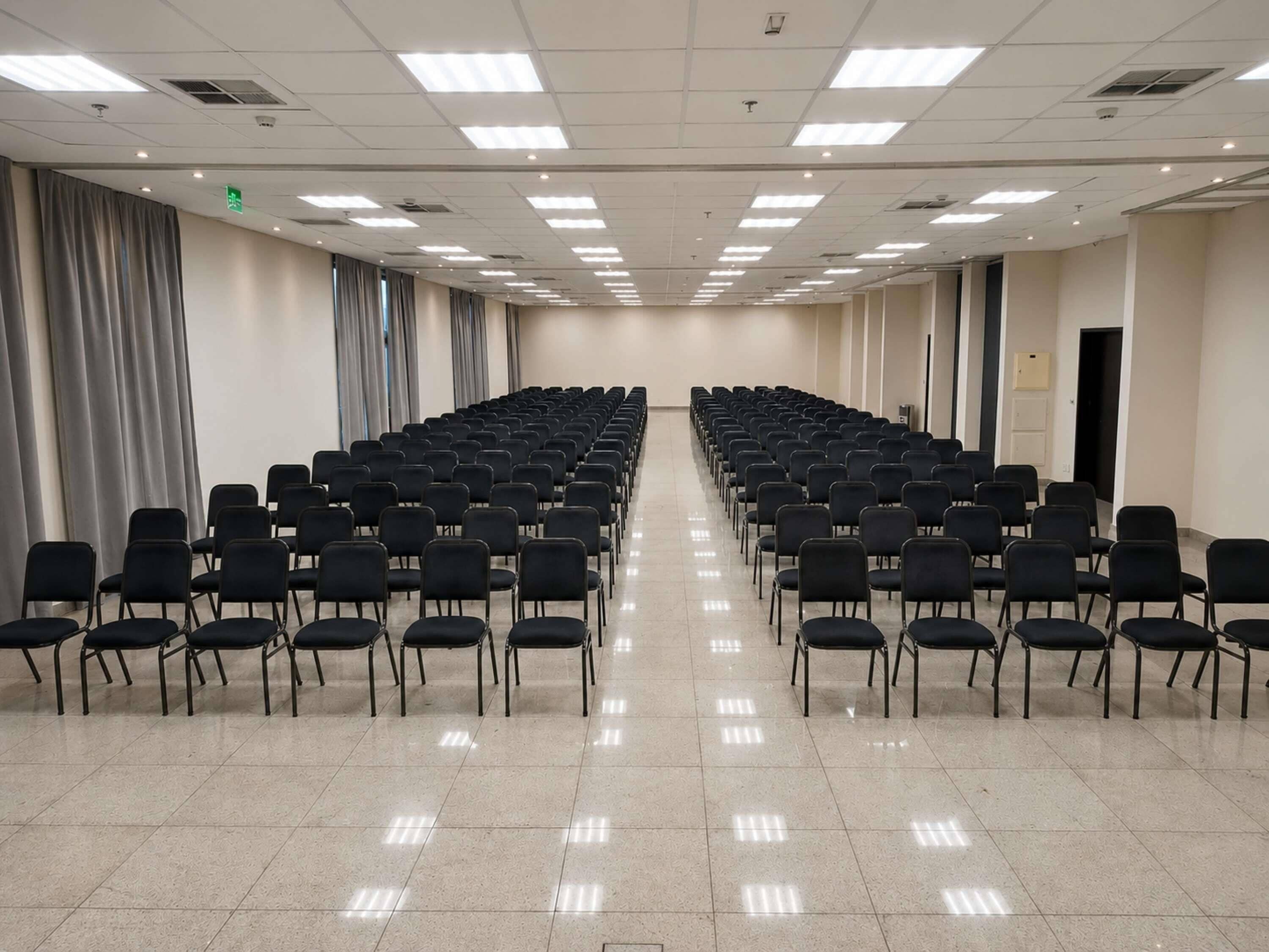 A conference room with rows of black chairs, a tiled floor, and ceiling lights.