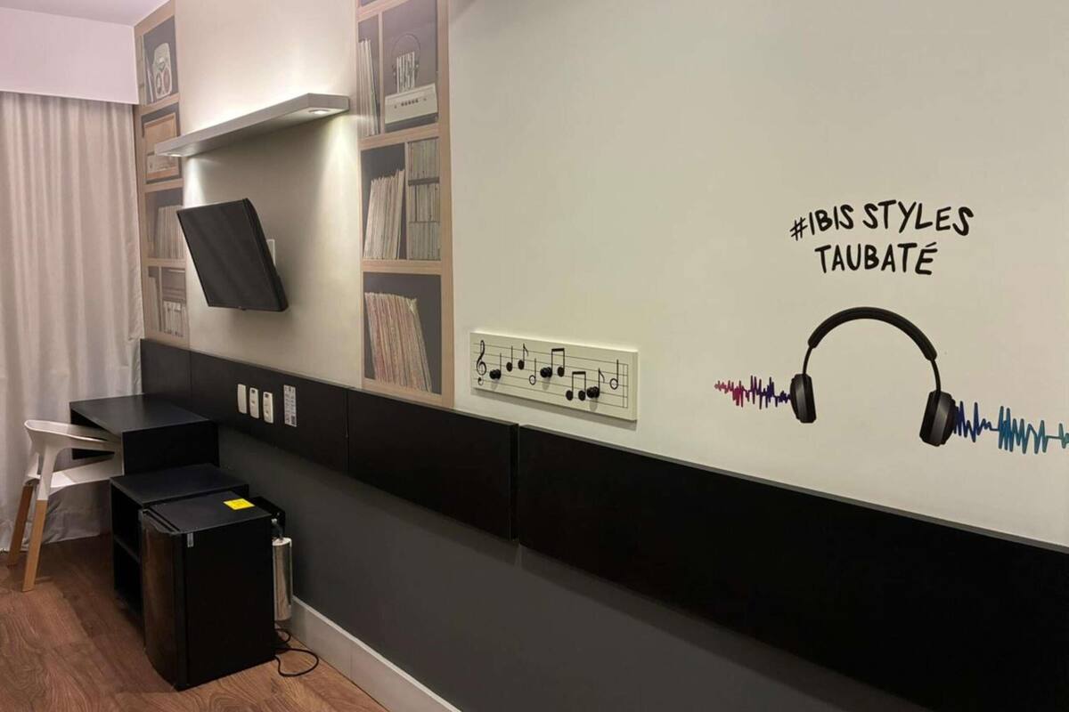 Une chambre moderne équipée d’un téléviseur à écran plat, d’une étagère remplie de livres, d’un lecteur de musique fixé au mur et d’un panneau affichant un hashtag.