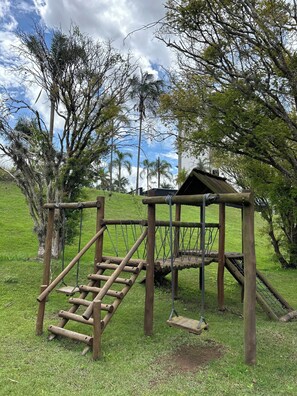 A wooden playground structure with a slide and climbing elements, surrounded by grass and trees. - Ibis Styles Taubate (Taubate)